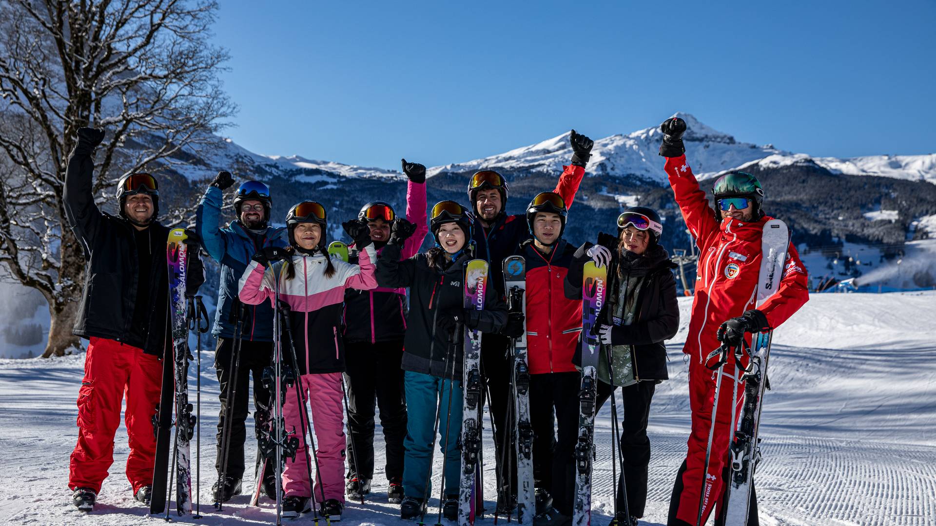 Group of skiers in helmets and goggles, holding skis on snowy mountain slope with clear sky.